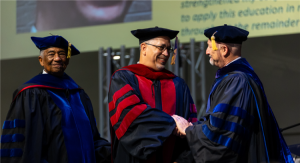 3 people standing inside in academic regalia shaking hands