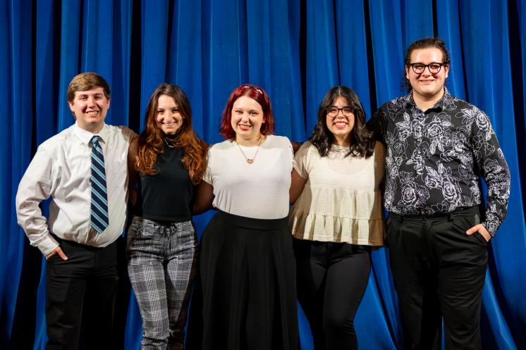 A group of five smiling people standing together in front of a blue curtain.