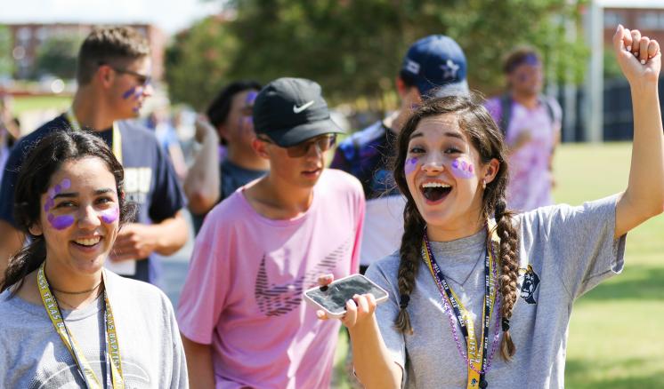 fall_2021_first_week_img_2 A group of young people smiling outdoors, with one holding a phone and raising their fist.
