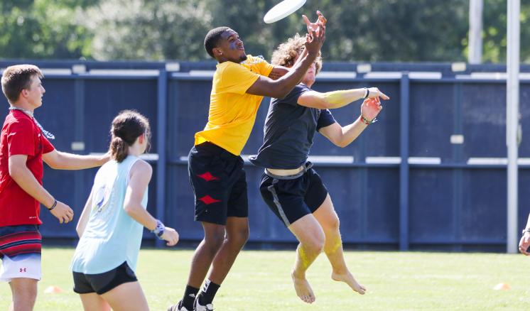 fall_2021_first_week_img_4 Players leap for a frisbee during an Ultimate Frisbee game on a grassy field.