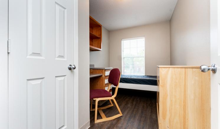 Small dorm room with a desk, chair, bed, and window.
