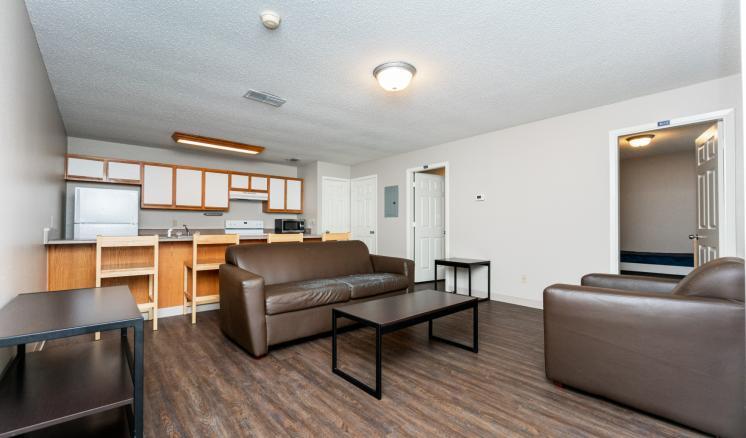 A modern living room with wooden flooring, brown leather furniture, a dark coffee table, and a light wooden dining set.
