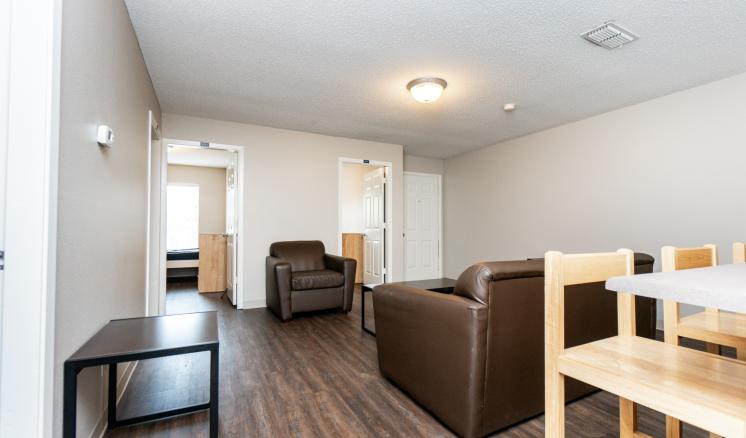 A modern living room with wooden flooring, brown leather furniture, a dark coffee table, and a light wooden dining set.