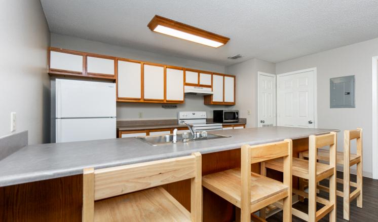 A modern kitchen with a gray countertop, wooden stools, and white appliances.