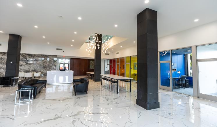 img_2 Modern lobby with glossy white marble floor, black leather seating, colorful paneling, and glass-walled office.
