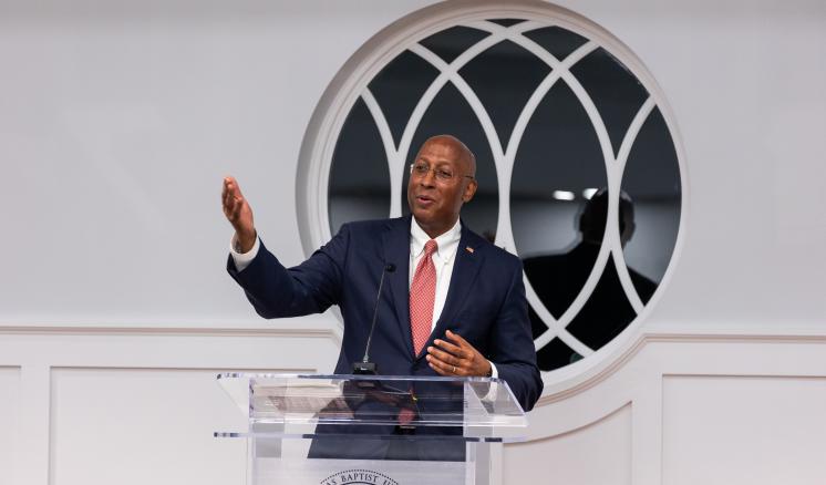 Man speaking behind podium with arm extended