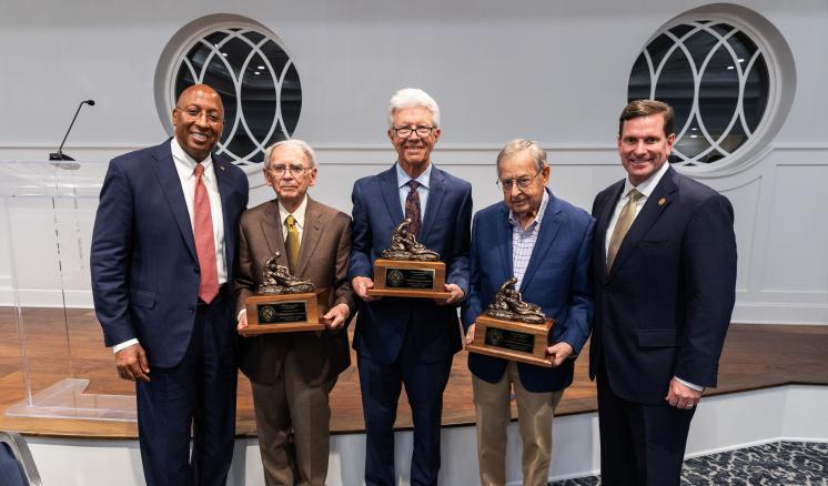 Three men holding awards in the center with two men on either side smiling at the camera