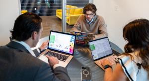 3 people sitting in a brightly lit room looking at laptops on the table