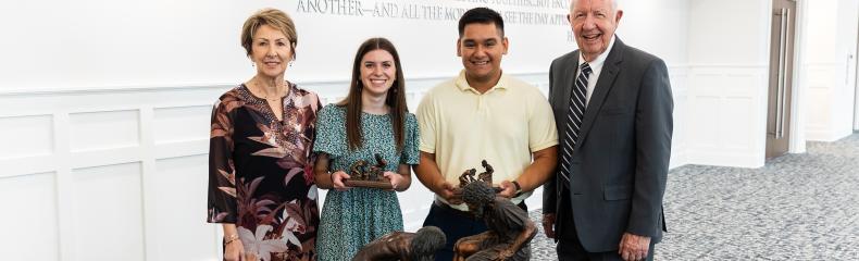 Avery Abshier and Abraham Contreras Two males and females standing in front of a table with a navy ETBU tablecloth and Jesus feet washing statue on the top of the table